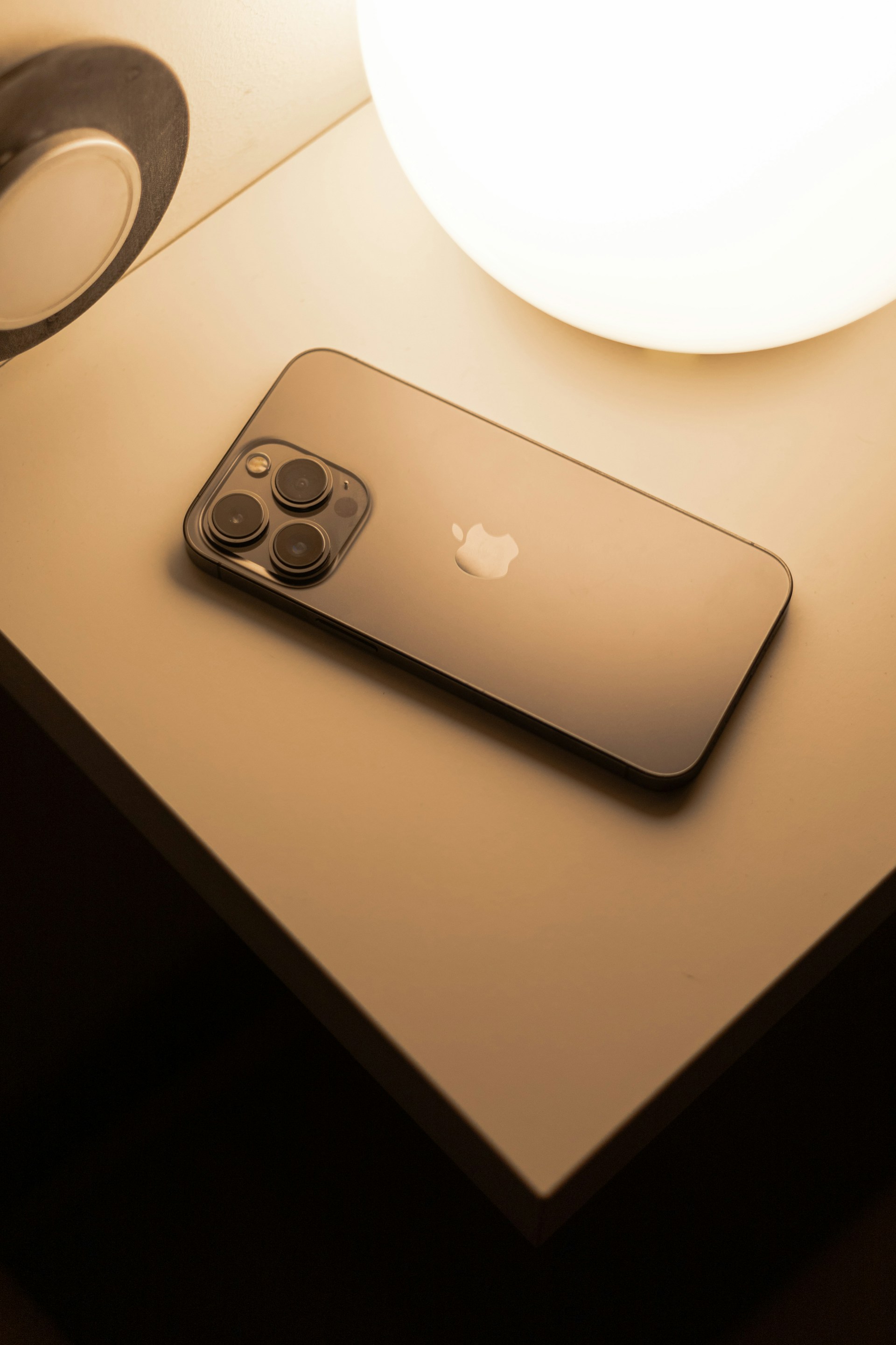 An iPhone resting on a nightstand beside a warm lamp.